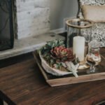 Uma bandeja de madeira apresenta uma vela e suculentas, criando um ambiente acolhedor e natural.
