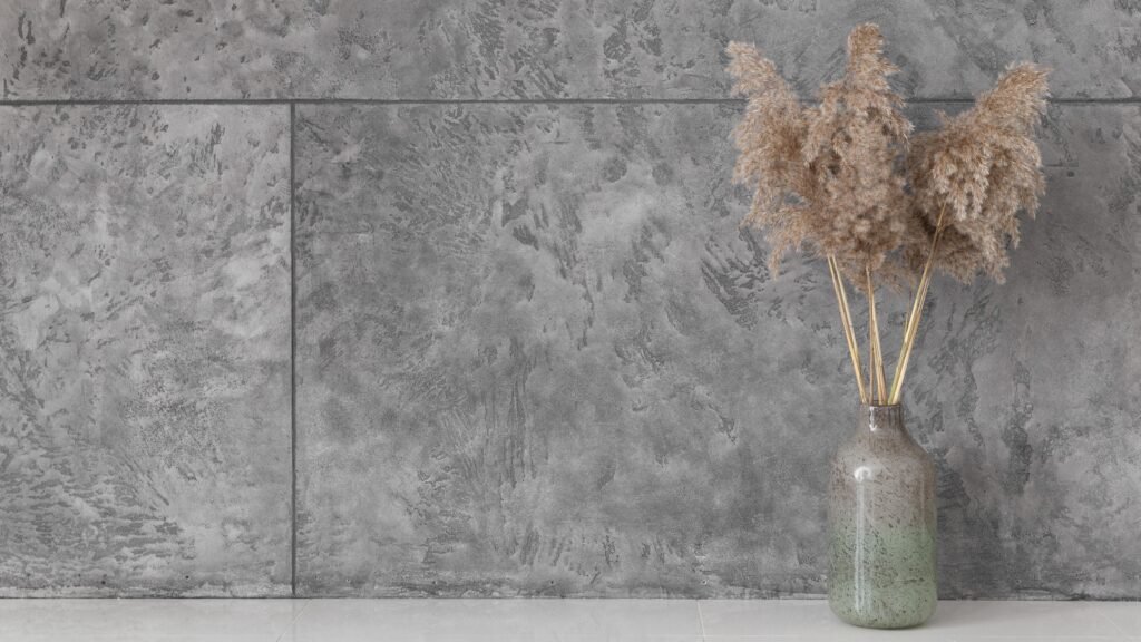Vaso decorativo com grama seca, localizado em frente a uma parede revestida de quartzo de cor cinza.